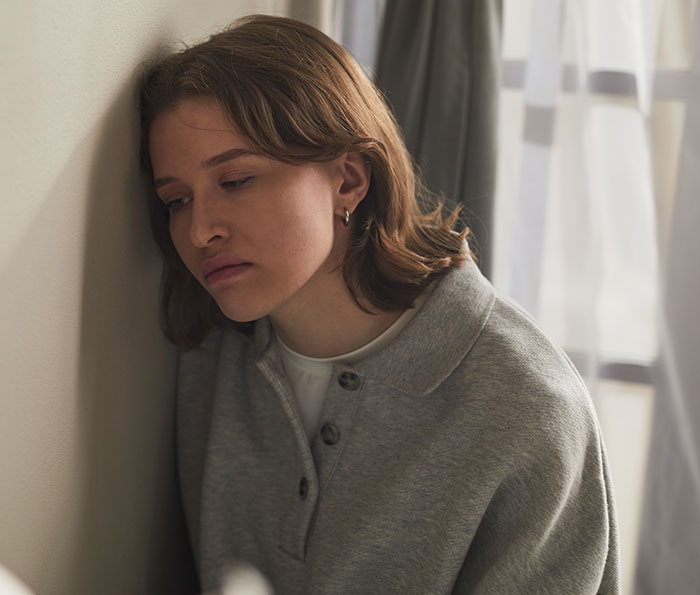 A person leans against a wall, looking sad, after being accused of buying stepson's love with gifts.
