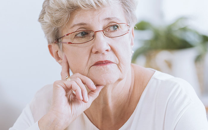 A thoughtful older woman wearing glasses, reflecting on accusations of buying her stepson's love with gifts.