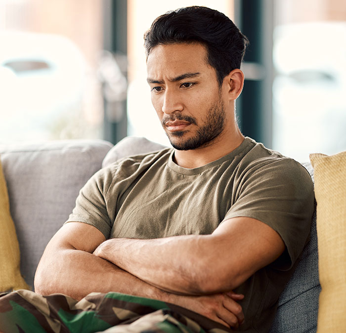 A man with a serious expression, arms crossed, on a couch, reflecting on a situation involving his stepson and gifts.