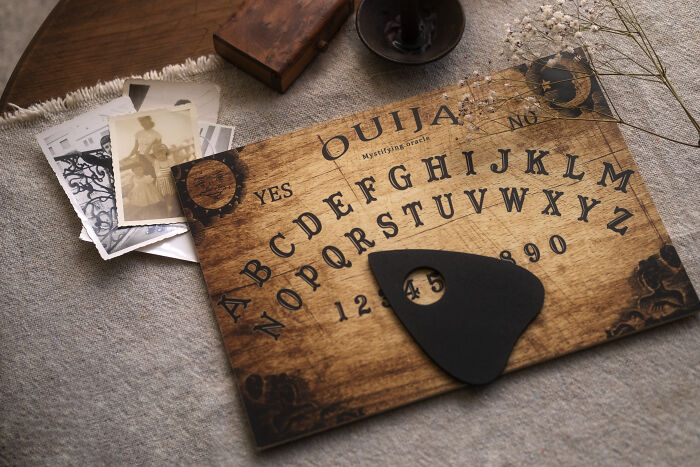 A Ouija board on a table with old photos, representing unhinged house rules that make sense to the family.