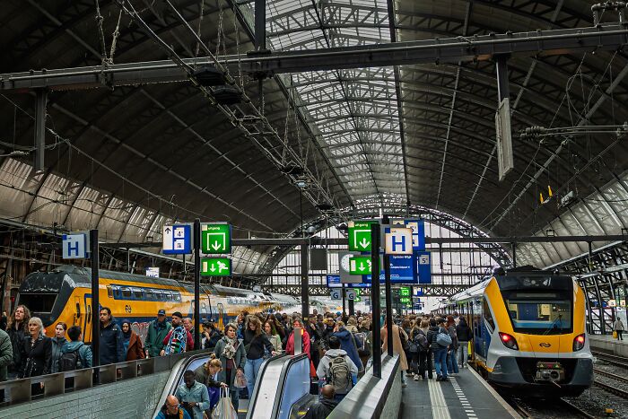 A busy train station with passengers and trains, depicting a travel scene with many tourists.