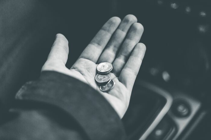 A hand holds a few coins, symbolizing monetary exchanges during embarrassing encounters with American tourists.