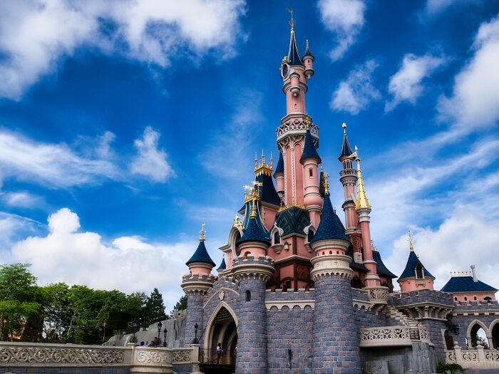 A fairytale castle with pink spires and blue roofs against a cloudy sky, a common sight for American tourists.