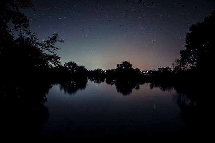 A dark, starry night sky over a tranquil lake with tree silhouettes, illustrating a serene scene for recalling weird encounters.