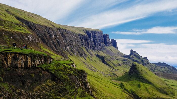 Majestic green mountains and steep cliffs under a blue sky, ideal for tourists to explore.