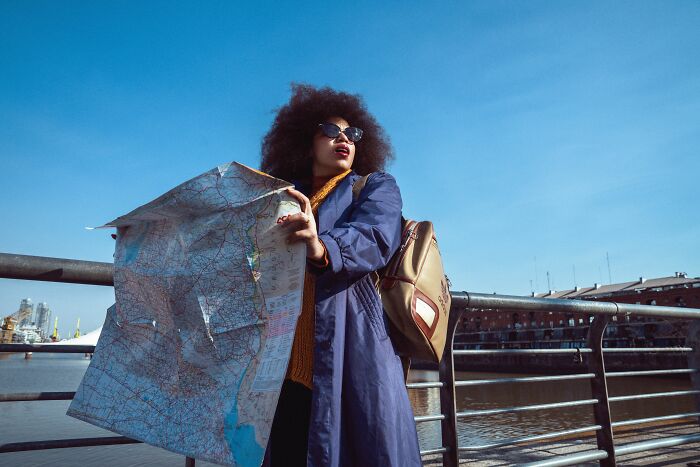 A female tourist with an afro hairstyle and sunglasses, holding a map, experiencing weird encounters.