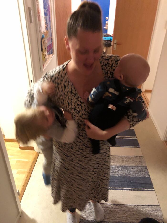 A mom looks overwhelmed but happy while holding two babies, reflecting the rewarding and not easy aspects of motherhood.