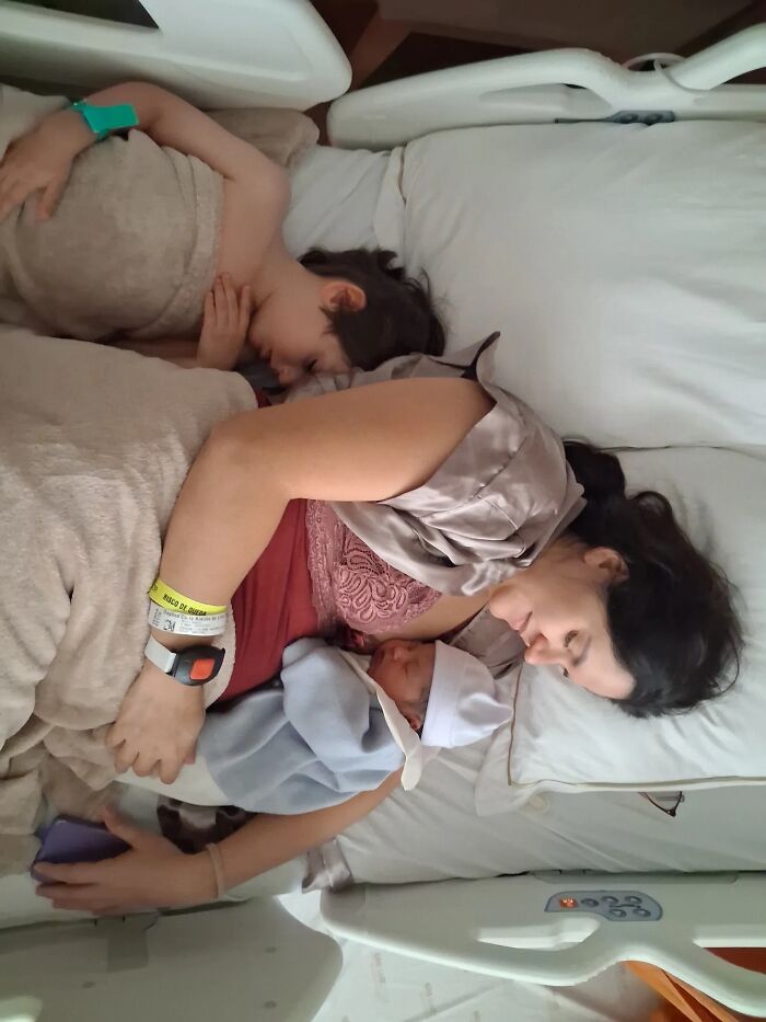 A mom with her two young children, including a newborn, sleeping peacefully together in a hospital bed, showing rewarding motherhood.