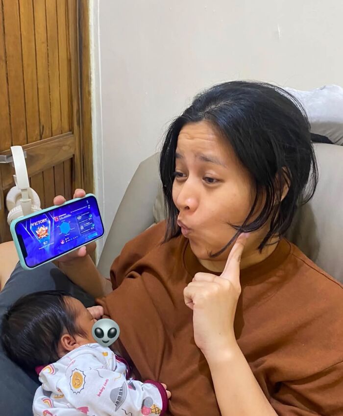 A mom holding her baby, playfully posing while looking at her phone, showcasing the rewarding moments of motherhood.