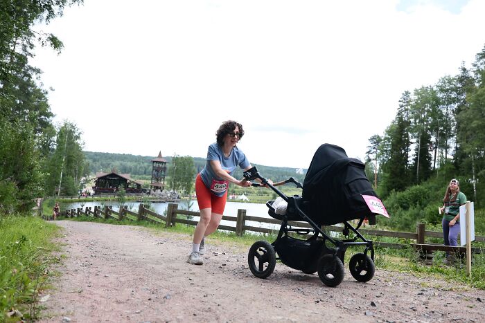 A mom pushes a stroller on a dirt path during what appears to be a race, showcasing the rewarding and active side of motherhood.