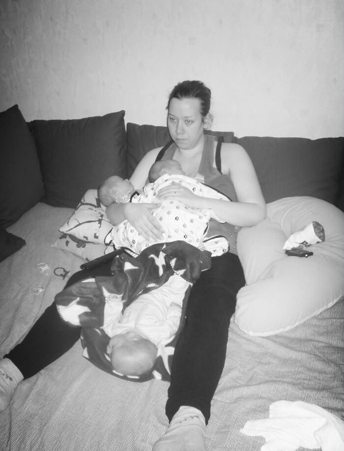 A tired mom with two infants on a bed, embodying the challenging yet fulfilling aspect of motherhood.