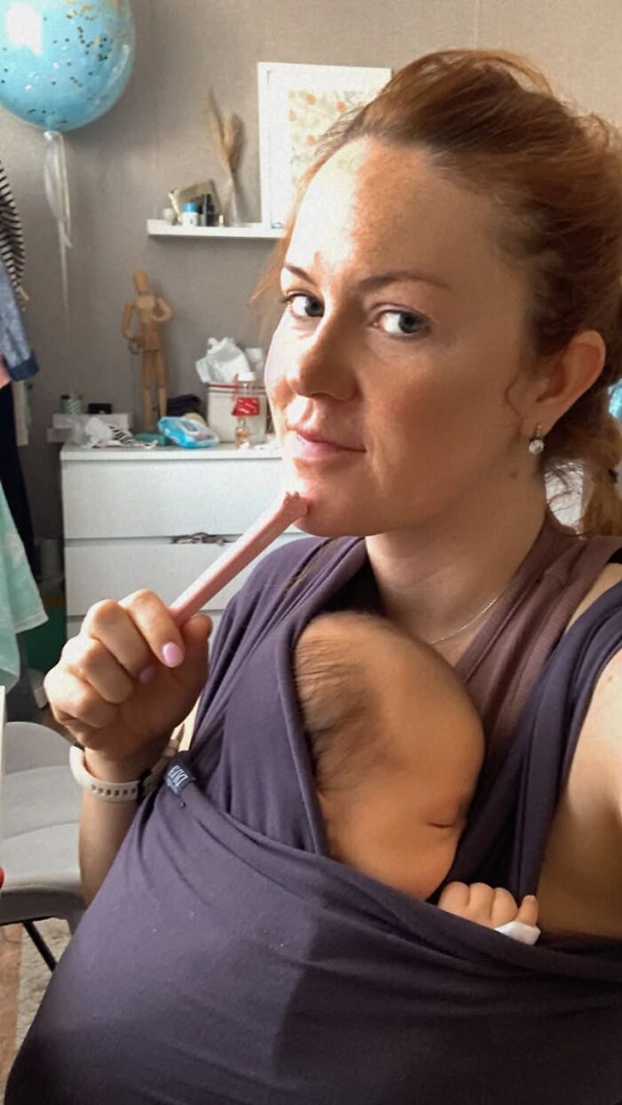 A mom with a baby in a carrier, multitasking with a hair tool, showcasing the challenging aspects of motherhood.