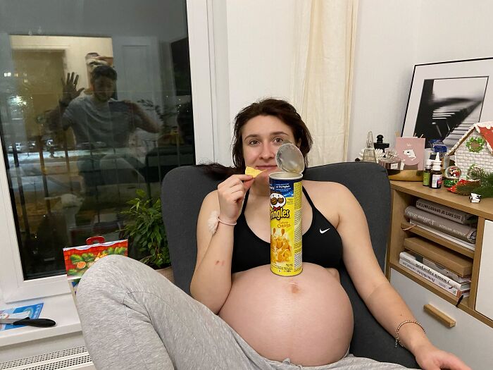 A pregnant woman enjoying chips, reflecting the rewarding aspects of motherhood, not always easy.