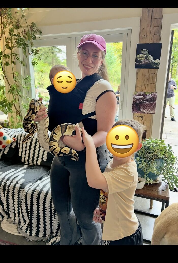 A mom holding a baby in a carrier and a snake, with a child beside her, depicting the varied experiences of motherhood.