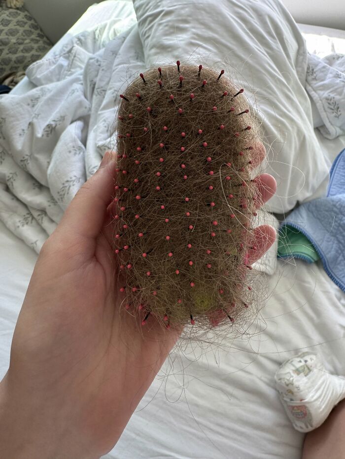 A hand holding a hairbrush full of hair, symbolizing the often messy and not easy reality of motherhood.