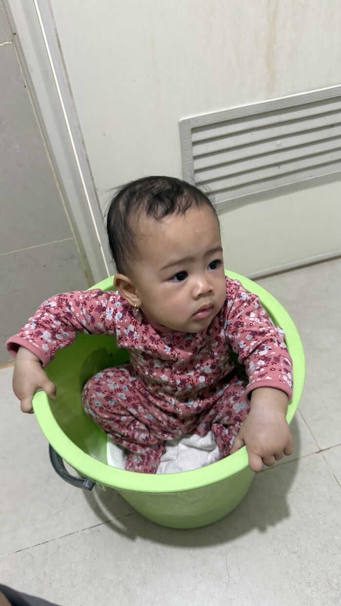 A baby sitting inside a green bucket, a joyful and fulfilling moment in motherhood.