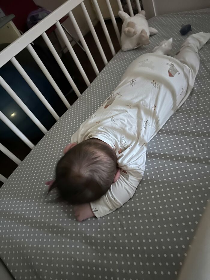 A baby sleeping on its stomach in a crib, depicting a quiet moment in motherhood.