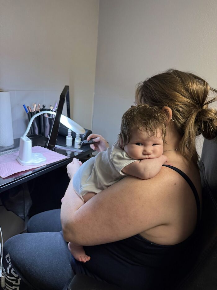A mom holding her baby over her shoulder while working at a desk, illustrating that motherhood is not easy but fulfilling.