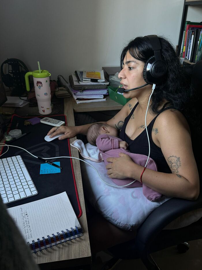 A mom wearing a headset works at a computer, holding her baby while multitasking; motherhood is not easy.