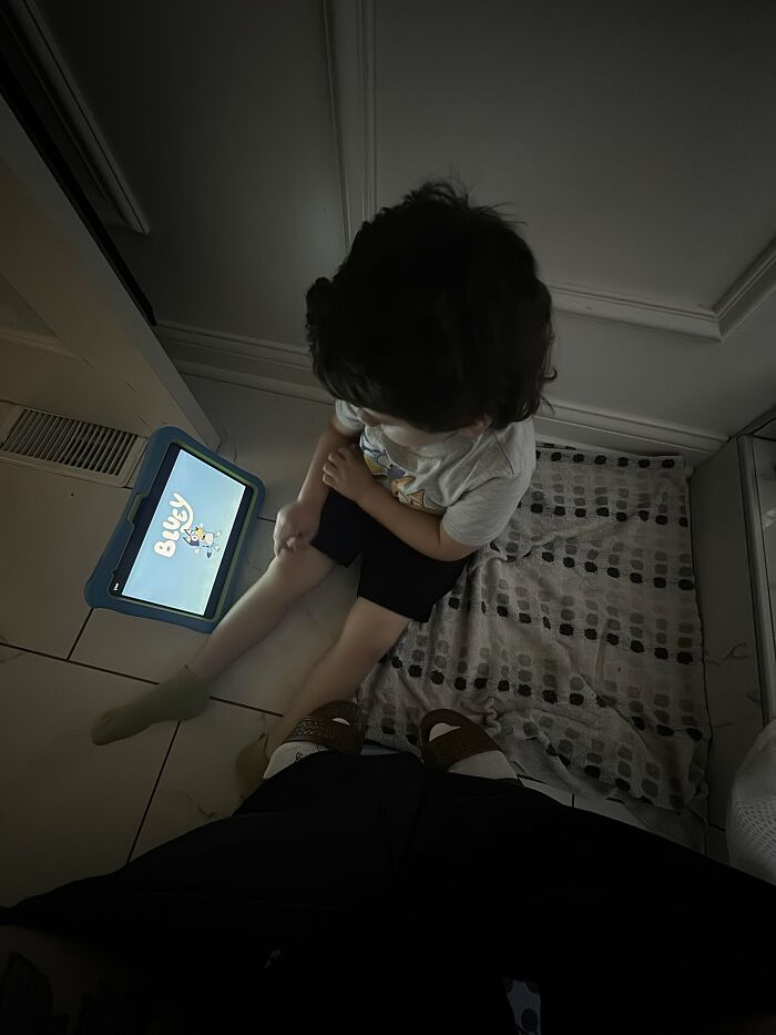 A child sits on the floor watching a tablet next to an adult, representing the rewarding and sometimes challenging moments of motherhood.