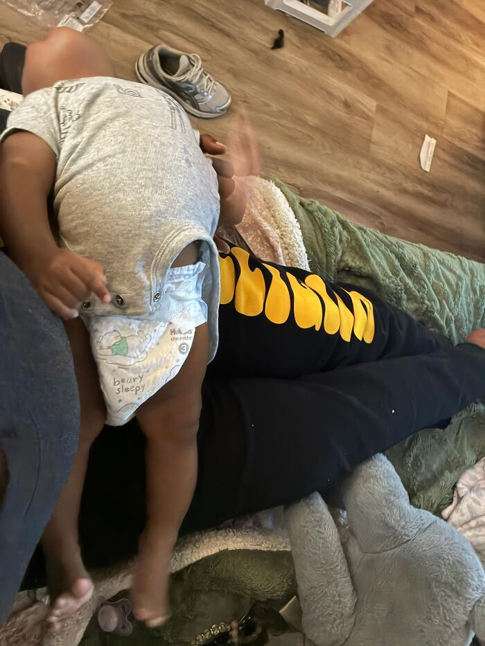 A baby in a diaper sleeps on an adults lap, illustrating the fulfilling but not always easy parts of motherhood.