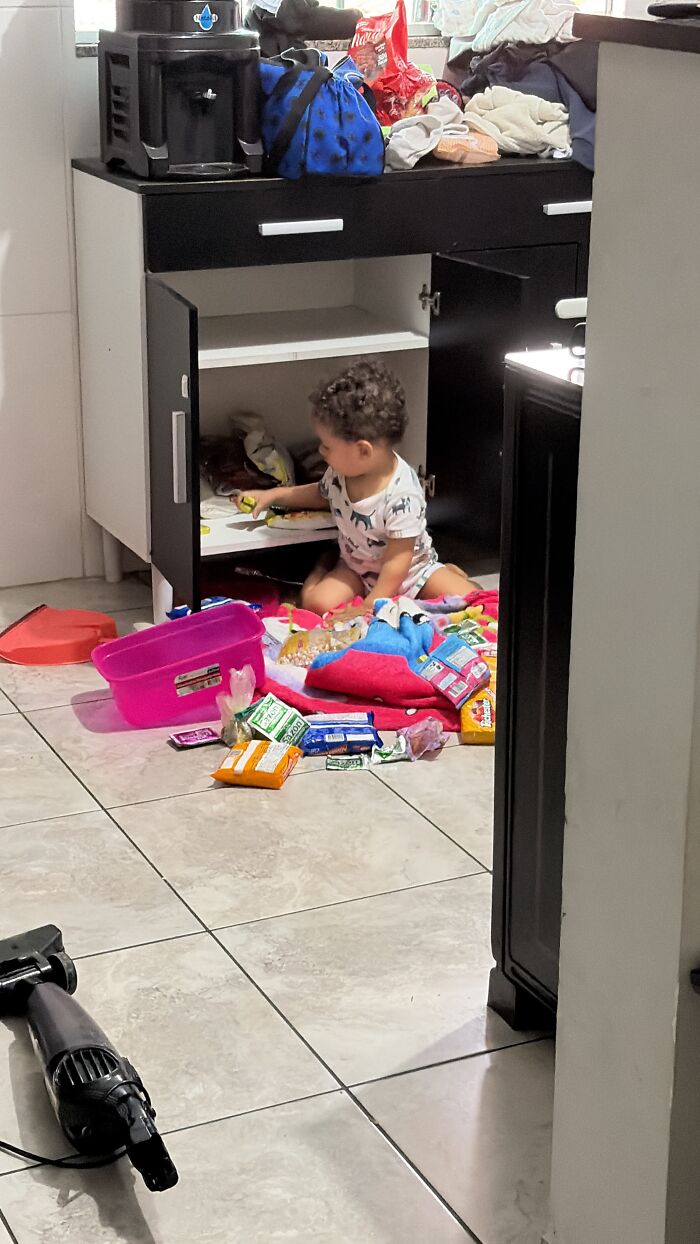 A baby explores an open cabinet, surrounded by items on the floor, reflecting the rewarding but not easy journey of motherhood.