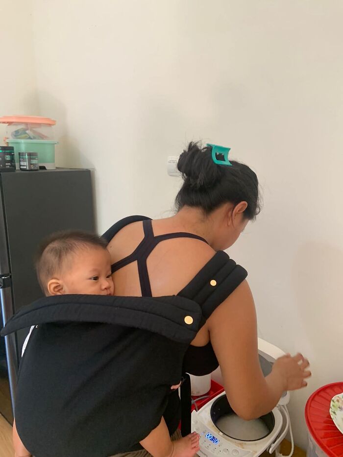 A mother carries her baby in a black carrier while attending to tasks, showcasing the joyful and fulfilling aspects of motherhood.