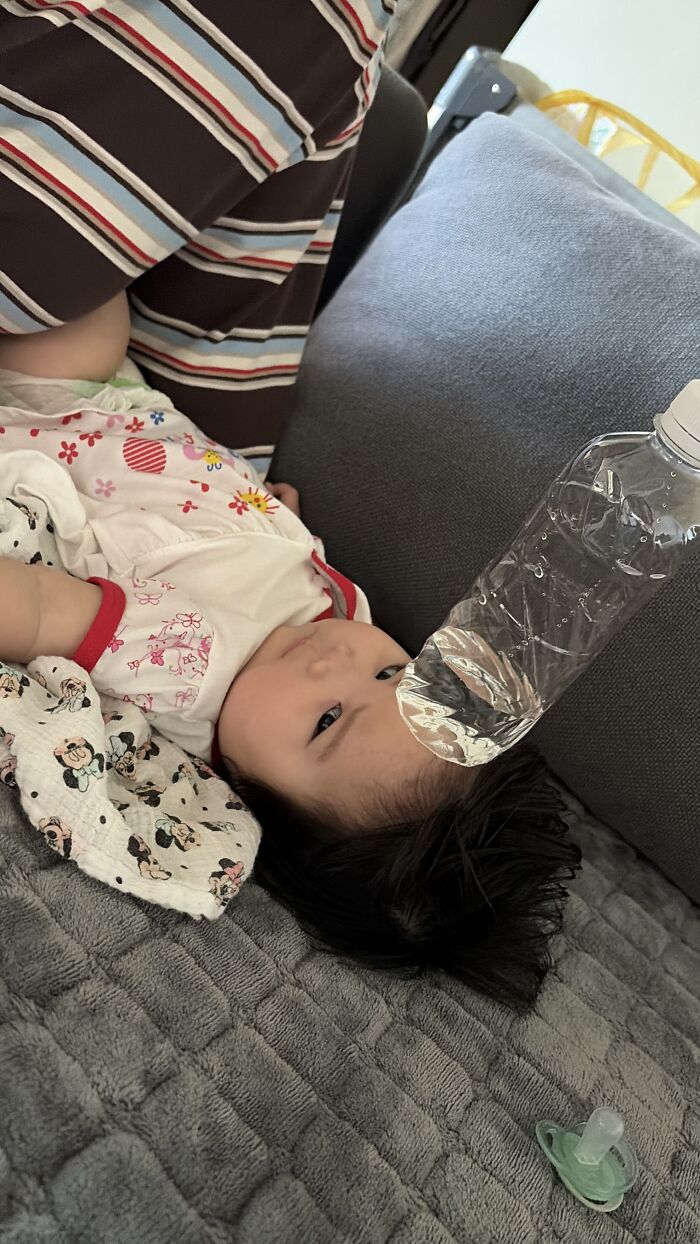 A baby lies on a couch, looking at a water bottle, embodying the everyday moments of motherhood.