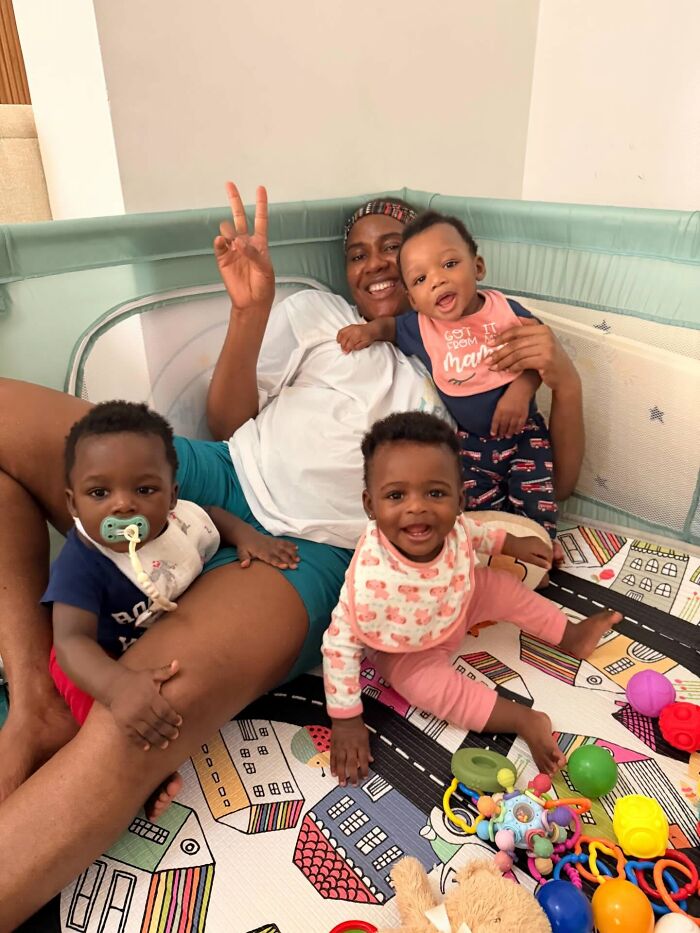 A happy mom poses with three babies in a playpen, illustrating the rewarding and joyful side of motherhood.