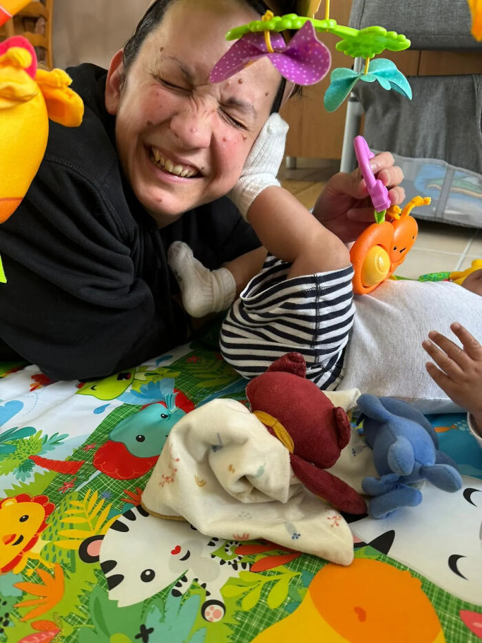 A mom smiles widely while playing with her baby on a colorful mat, showcasing the joyful and fulfilling aspects of motherhood.