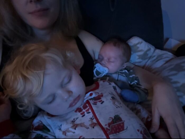 A mom cuddling with her two sleeping children, a toddler and a newborn, illustrating the joyful and fulfilling aspects of motherhood.
