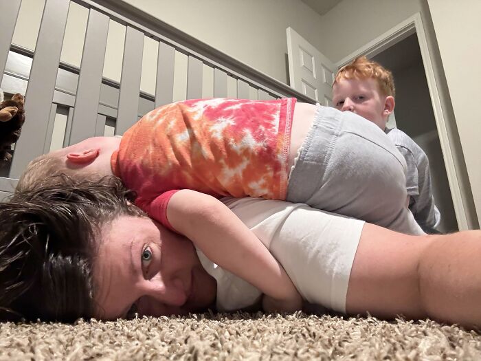 Motherhood is rewarding: A mom lying on the floor with her child on her back, highlighting the not easy, but joyful parts.
