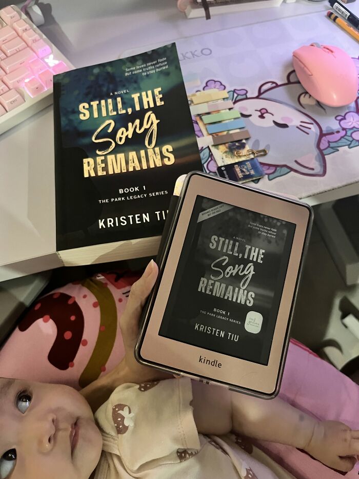 A mom holds a Kindle displaying Still, The Song Remains while cradling her baby, showcasing motherhood moments.