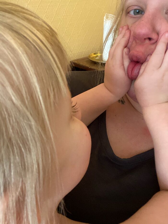 A toddler pokes their mom's face, making her stick out her tongue, showing a joyful moment of motherhood.