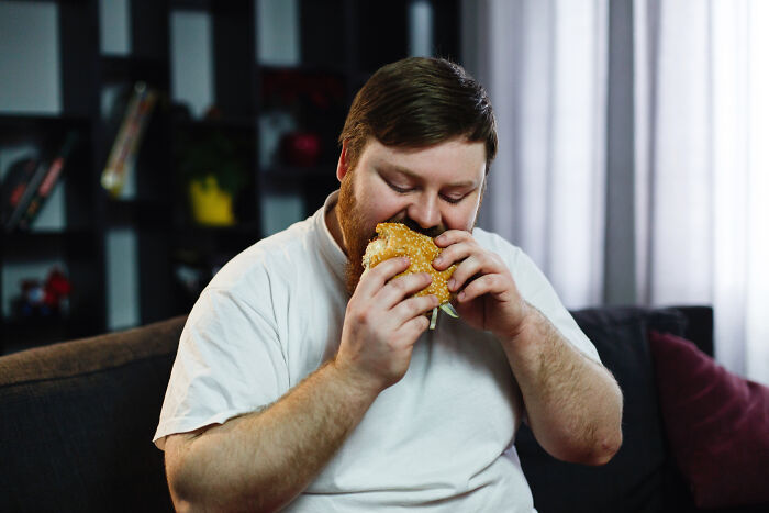 An overweight man enjoying a large burger, a hilarious and absurd moment of indulgence.
