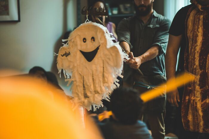 A ghost-shaped piñata is being held, with people gathered around for a hilarious celebration.
