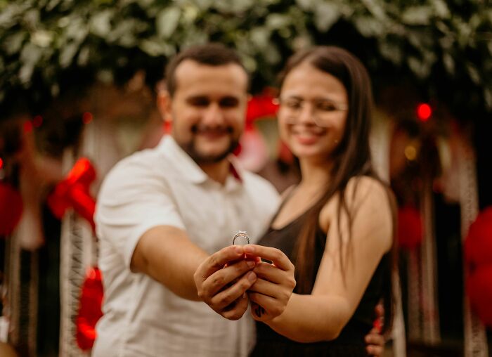 A couple holds up an engagement ring, celebrating. A firsthand witnessed moment of love, with possibly hilarious backstory.