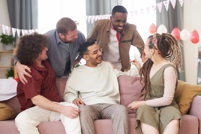 A diverse group of friends gathered on a couch, sharing a laugh and witnessing hilarious things firsthand.