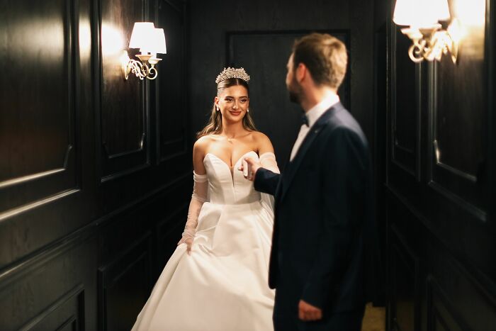 A smiling bride in a white dress and tiara holding hands with a groom, witnessing absurd and hilarious things.