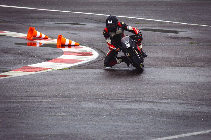 A motorcyclist leans into a wet turn, demonstrating an absurd and hilarious maneuver.