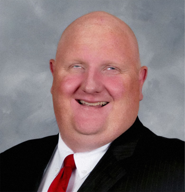 A bald man with a red tie smiling, from the not interesting community photos.