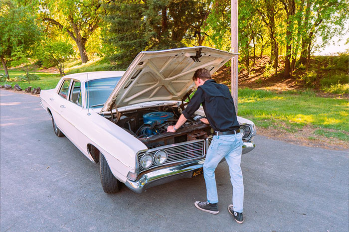 A resident inspects the engine of a classic white car, highlighting the secret scheme's uncovering.