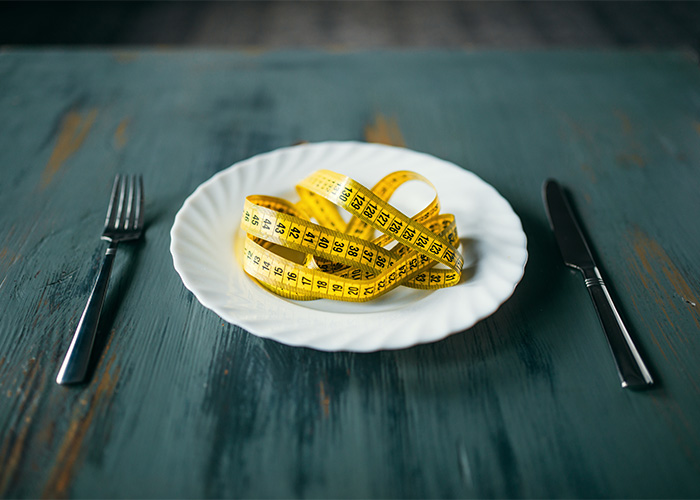 A measuring tape coiled on an empty plate, symbolizing extreme food habits and the debate surrounding them. A measuring tape coiled on an empty plate, symbolizing extreme food habits and the debate surrounding them.