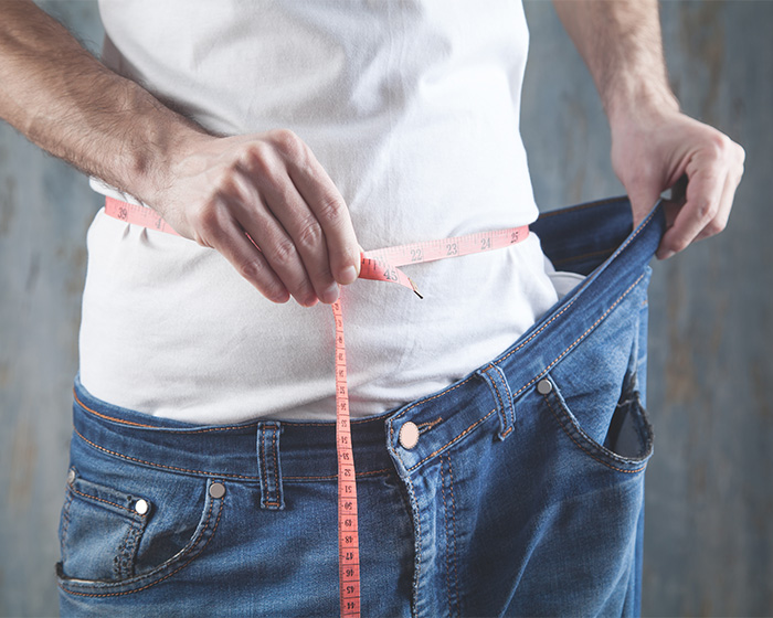 Man measuring his waist with a measuring tape, showing loose jeans. Hollywood star extreme food habits debate. Man measuring his waist with a measuring tape, showing loose jeans. Hollywood star extreme food habits debate.