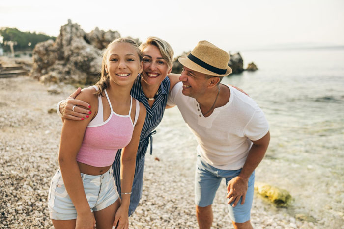 A family with a teen daughter on the beach smiling, representing a family after a violent fight.