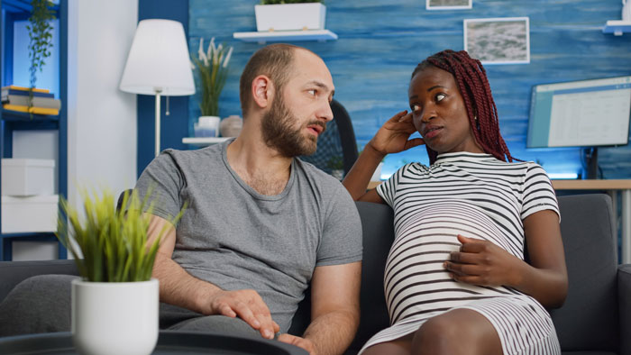A pregnant wife and her husband are deep in discussion on a couch, reflecting the tension over naming their daughter. A pregnant wife and her husband are deep in discussion on a couch, reflecting the tension over naming their daughter.