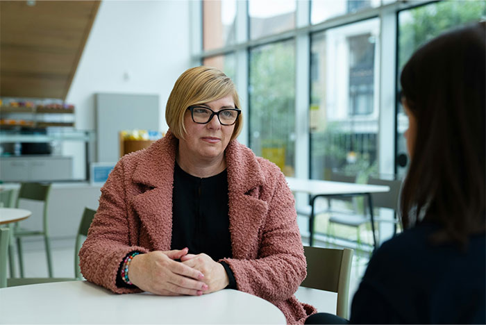 A woman in a pink coat sitting at a table, possibly discussing a woman waiting 25 years to apologize. A woman in a pink coat sitting at a table, possibly discussing a woman waiting 25 years to apologize.