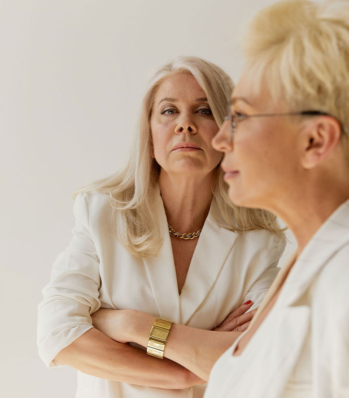 Two older women with serious expressions, one looking directly at the camera. Represents a woman apologizing for stealing a husband. Two older women with serious expressions, one looking directly at the camera. Represents a woman apologizing for stealing a husband.