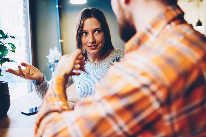 A woman with freckles looking at a man, gesturing with her hands in a hilariously awkward conversation. A woman with freckles looking at a man, gesturing with her hands in a hilariously awkward conversation.