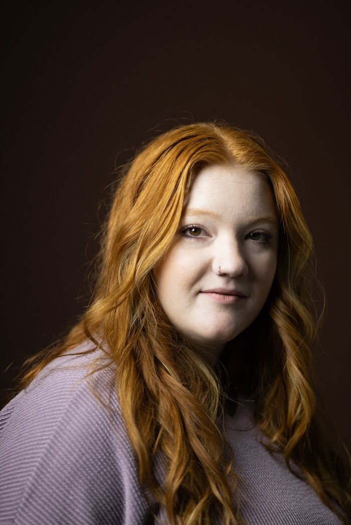 Portrait of a young natural redhead woman with long wavy hair, looking confidently for the portrait project.